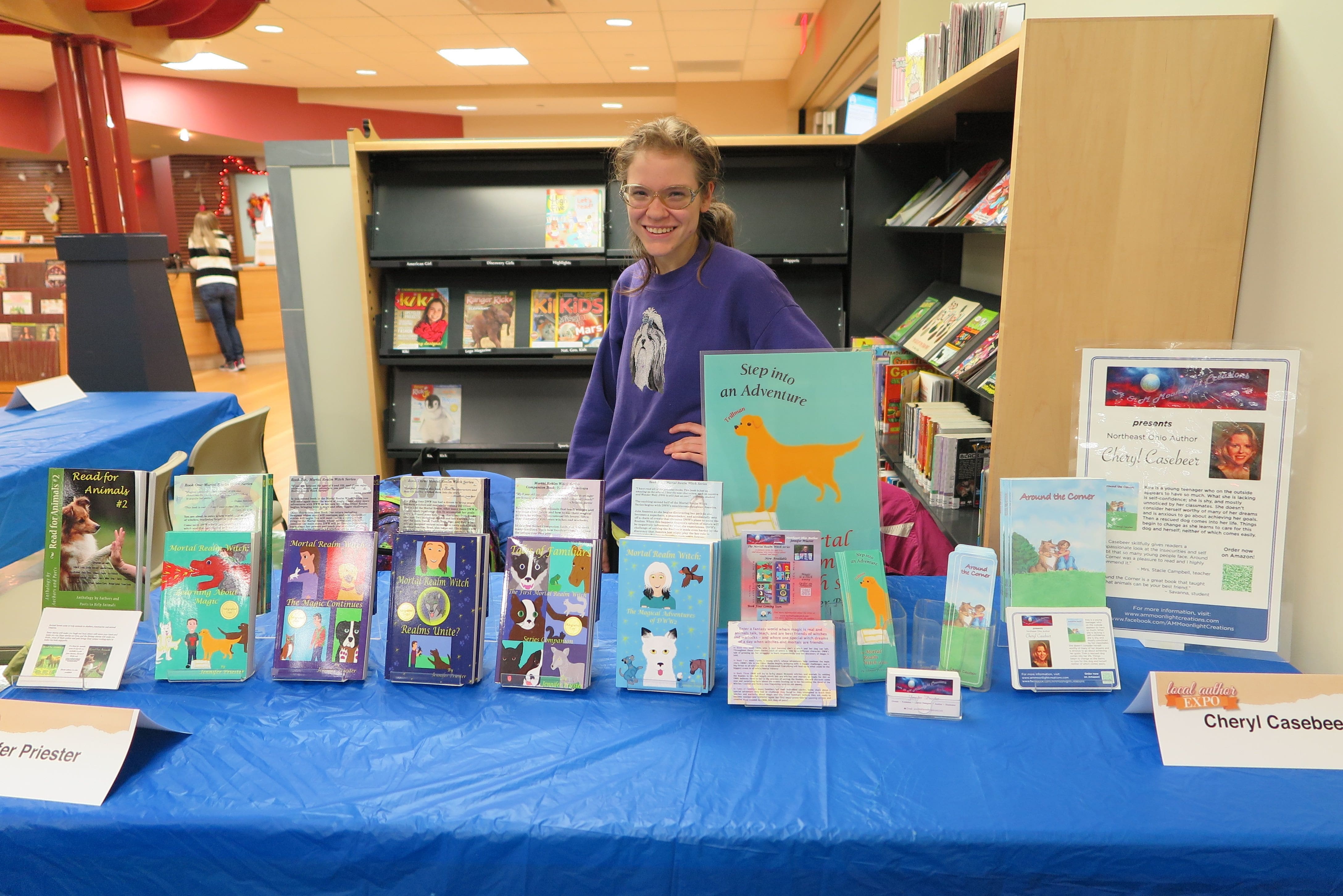 A photo of Jennifer Priester at an author event at a library with several of her books.