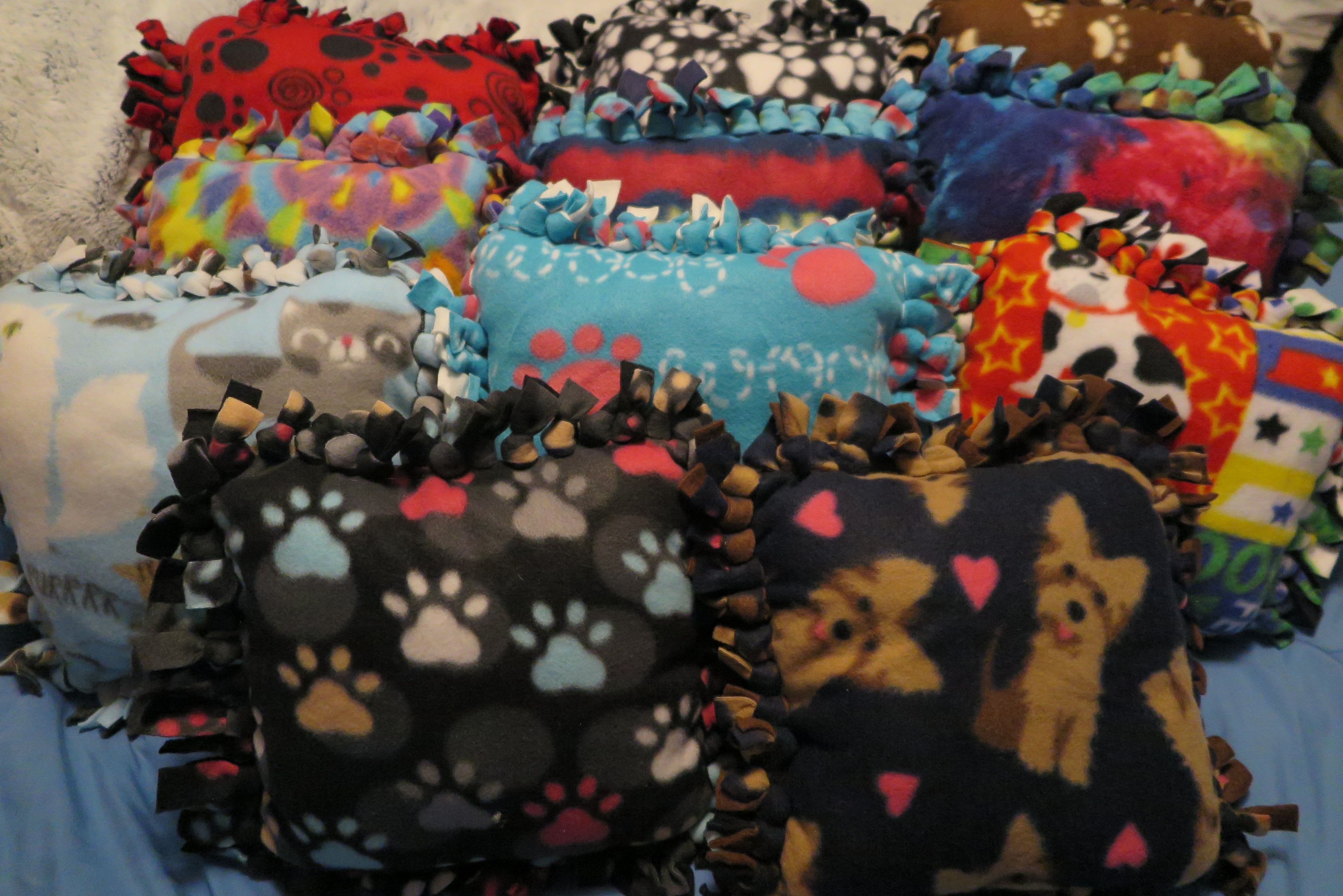 Handmade fringe pillows featuring various patterns. Paw print patterns, a dog pattern, and a rainbow tie dye pattern are visible.